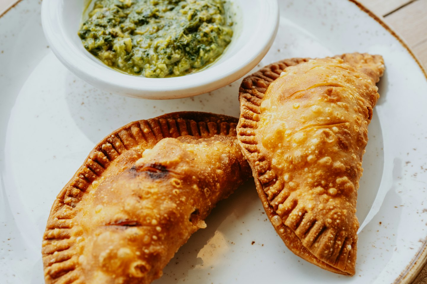 Two golden fried empanadas served with a bowl of green sauce.