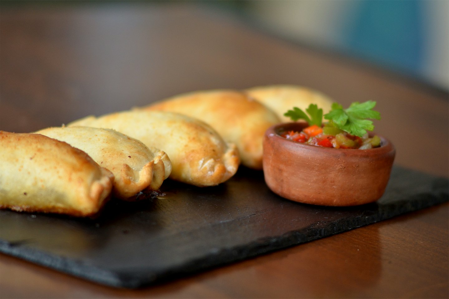 Golden empanadas and a bowl of salsa on a wooden table.