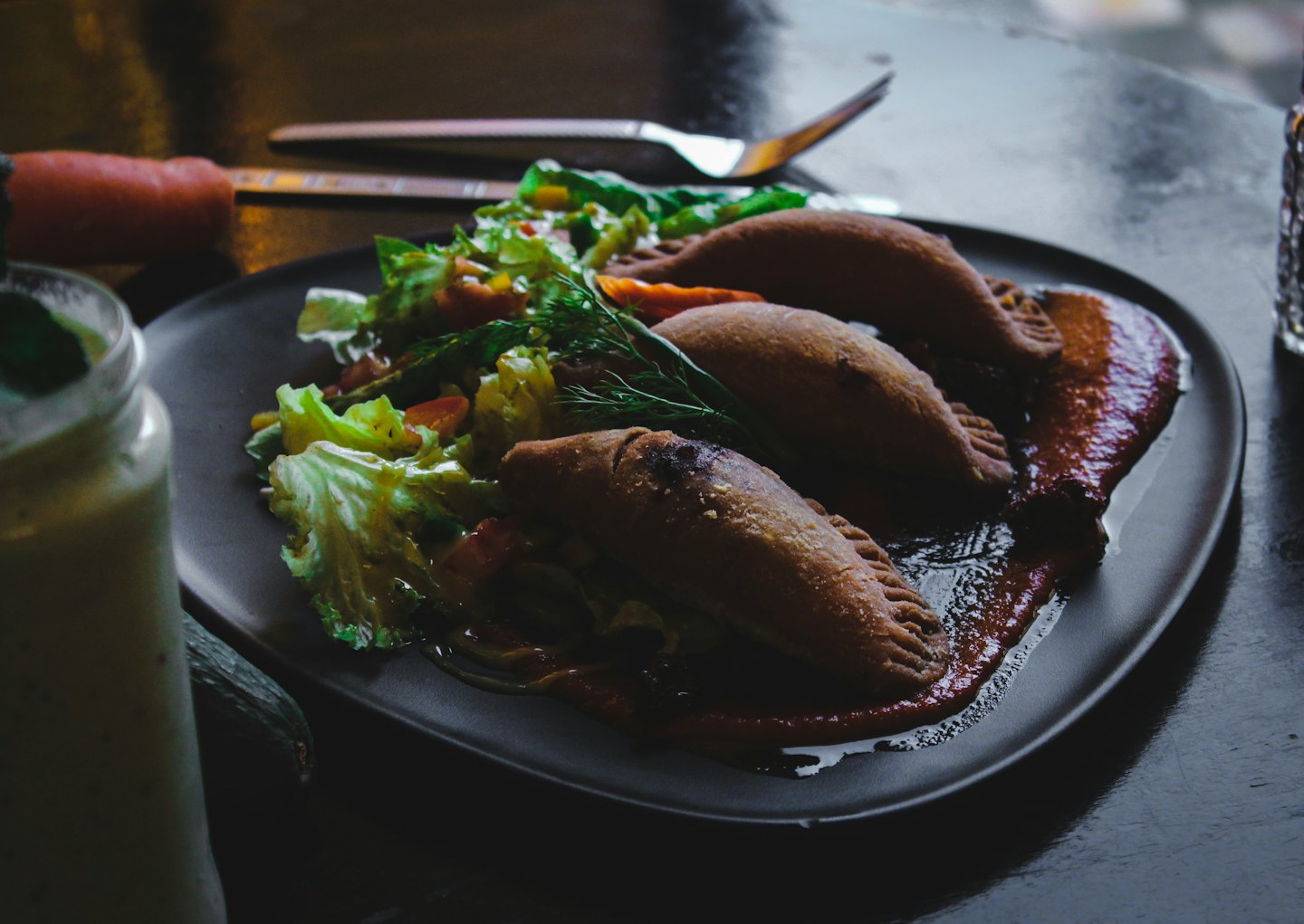 Three empanadas with a side salad and red sauce on a plate.