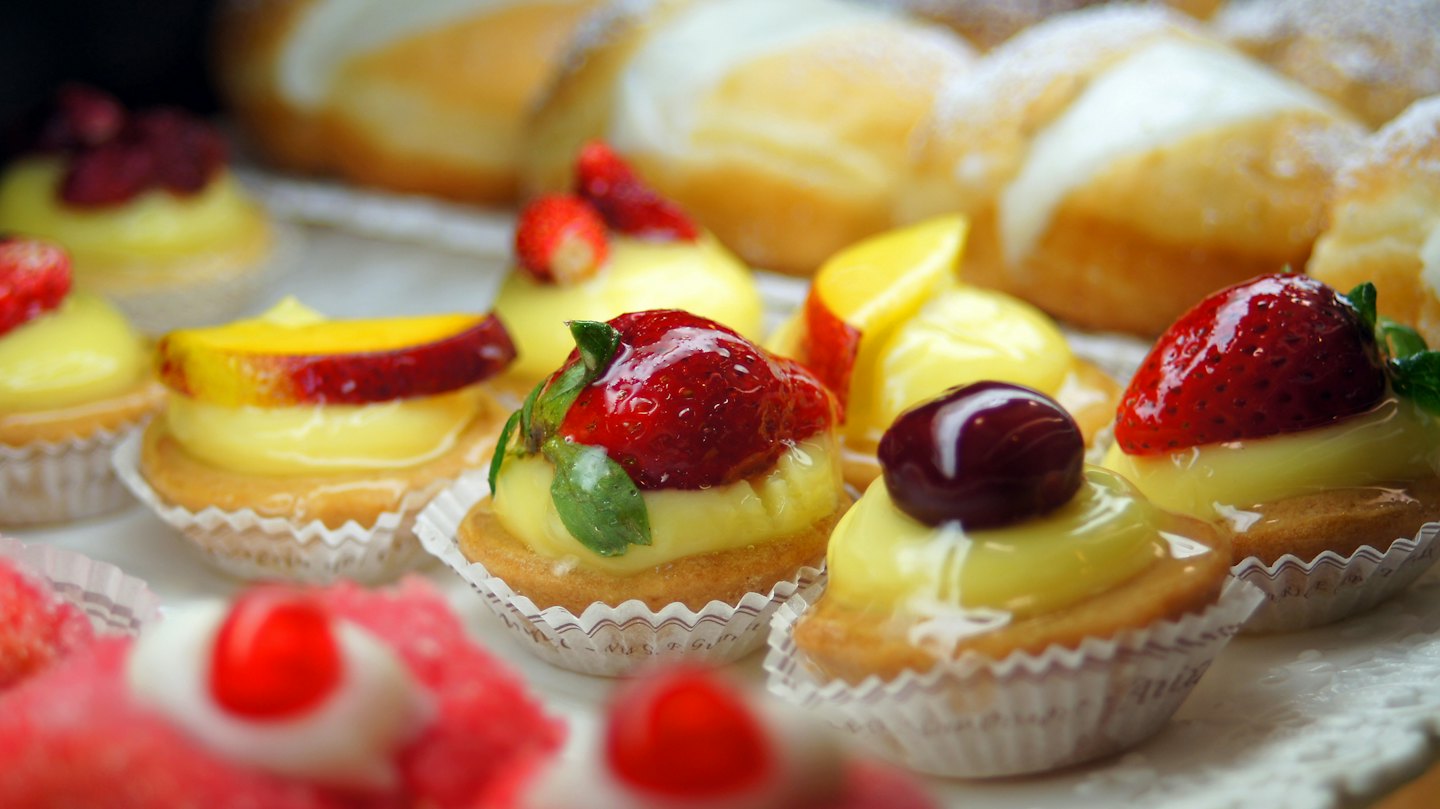 Mini fruit tarts topped with berries and peaches in a bakery.