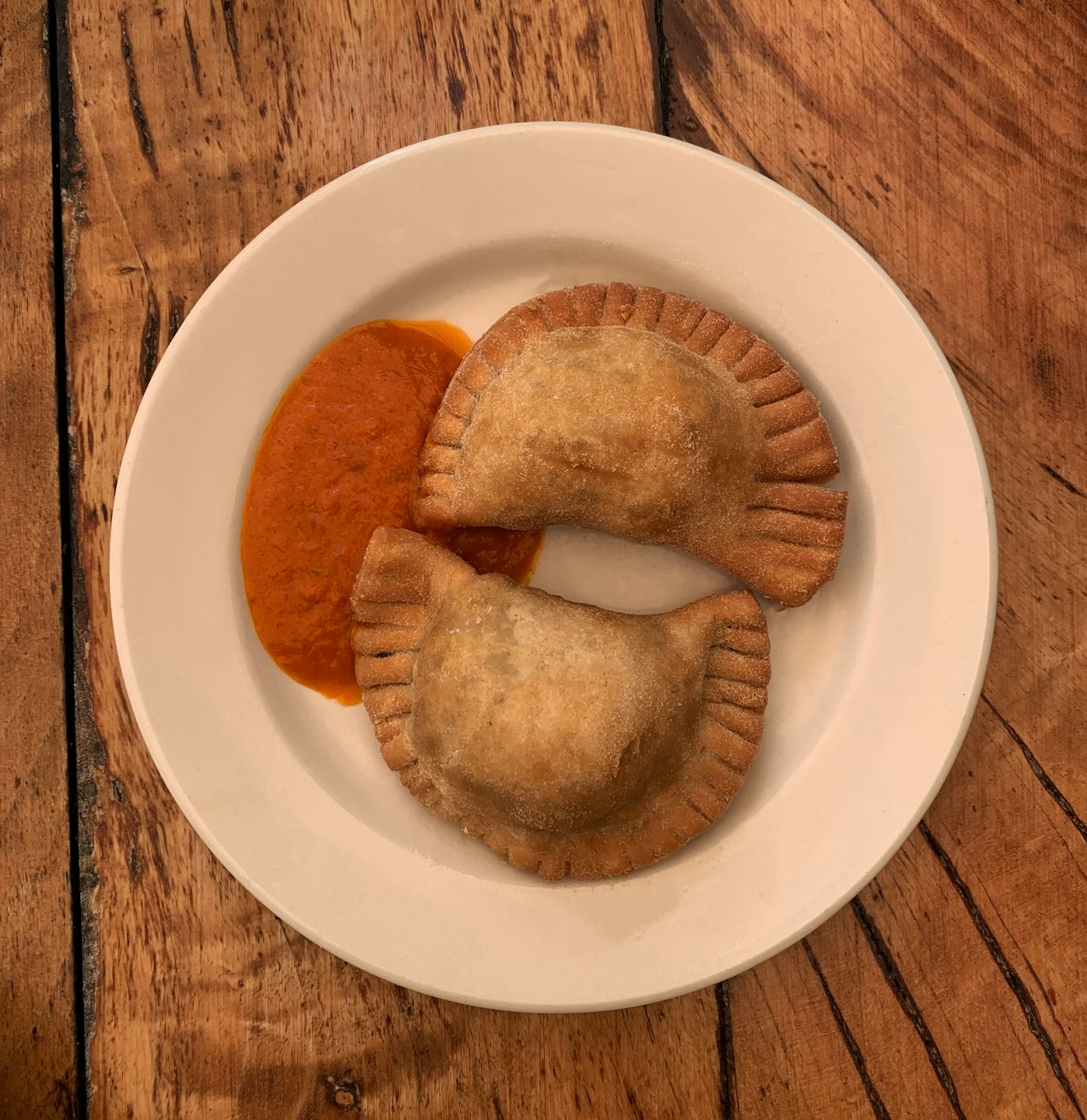 Two golden empanadas on a white plate with red sauce.
