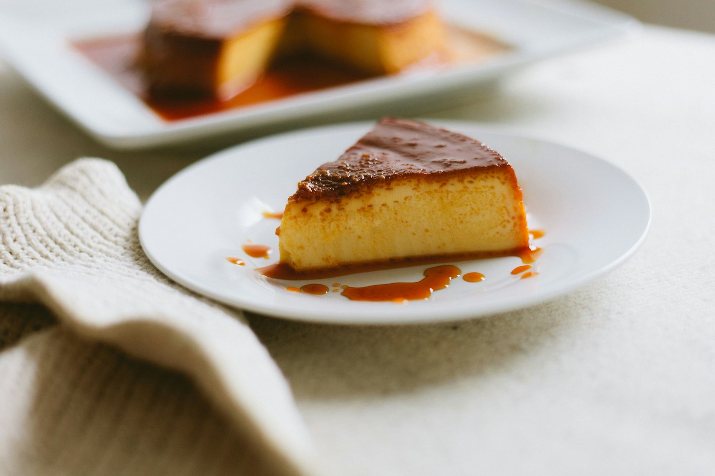 Slice of golden flan with caramel on a white plate.