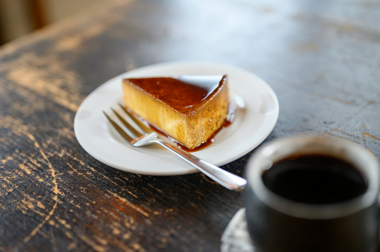 A slice of caramel flan served on a plate with a fork.