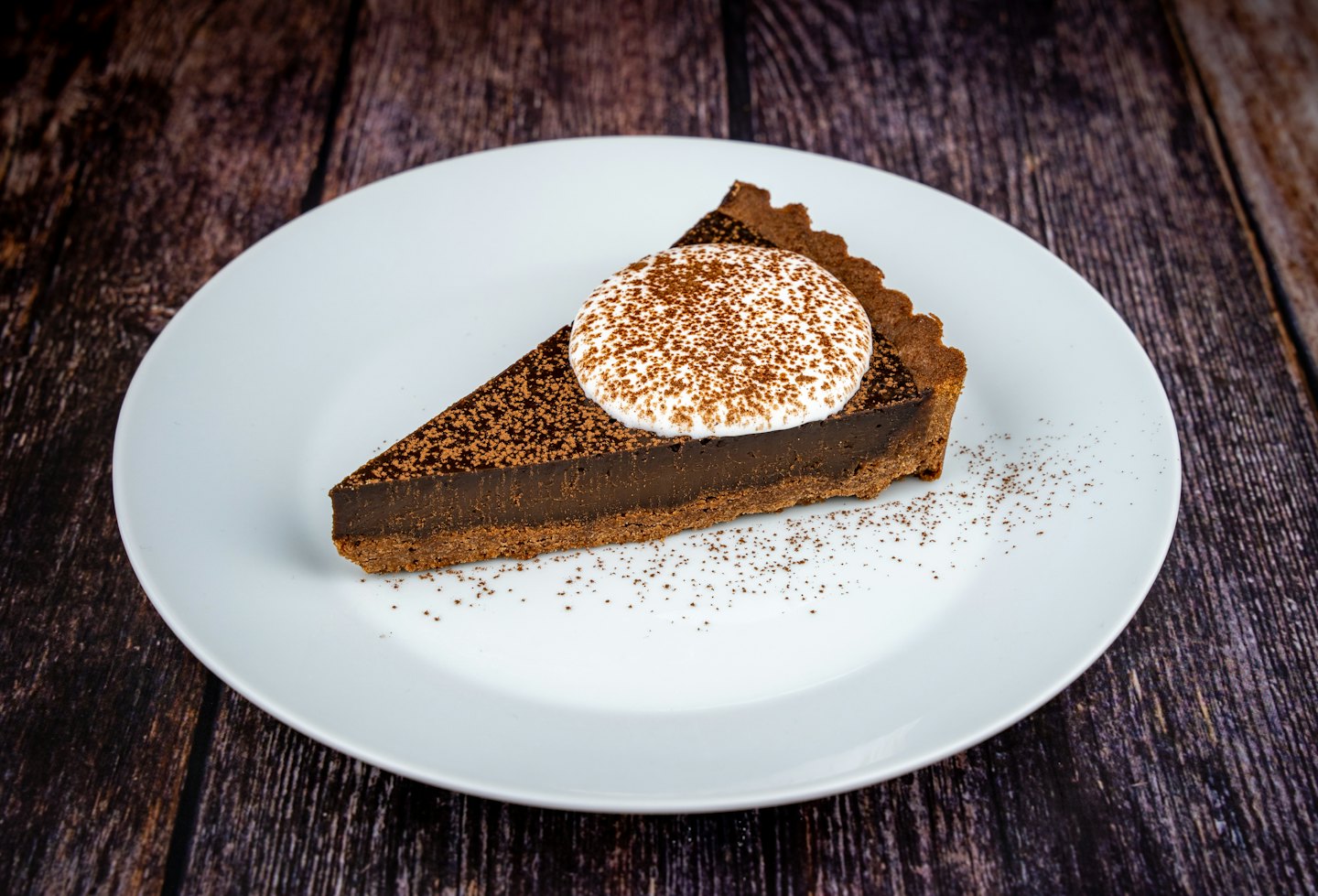 A slice of chocolate tart topped with cream on a plate.