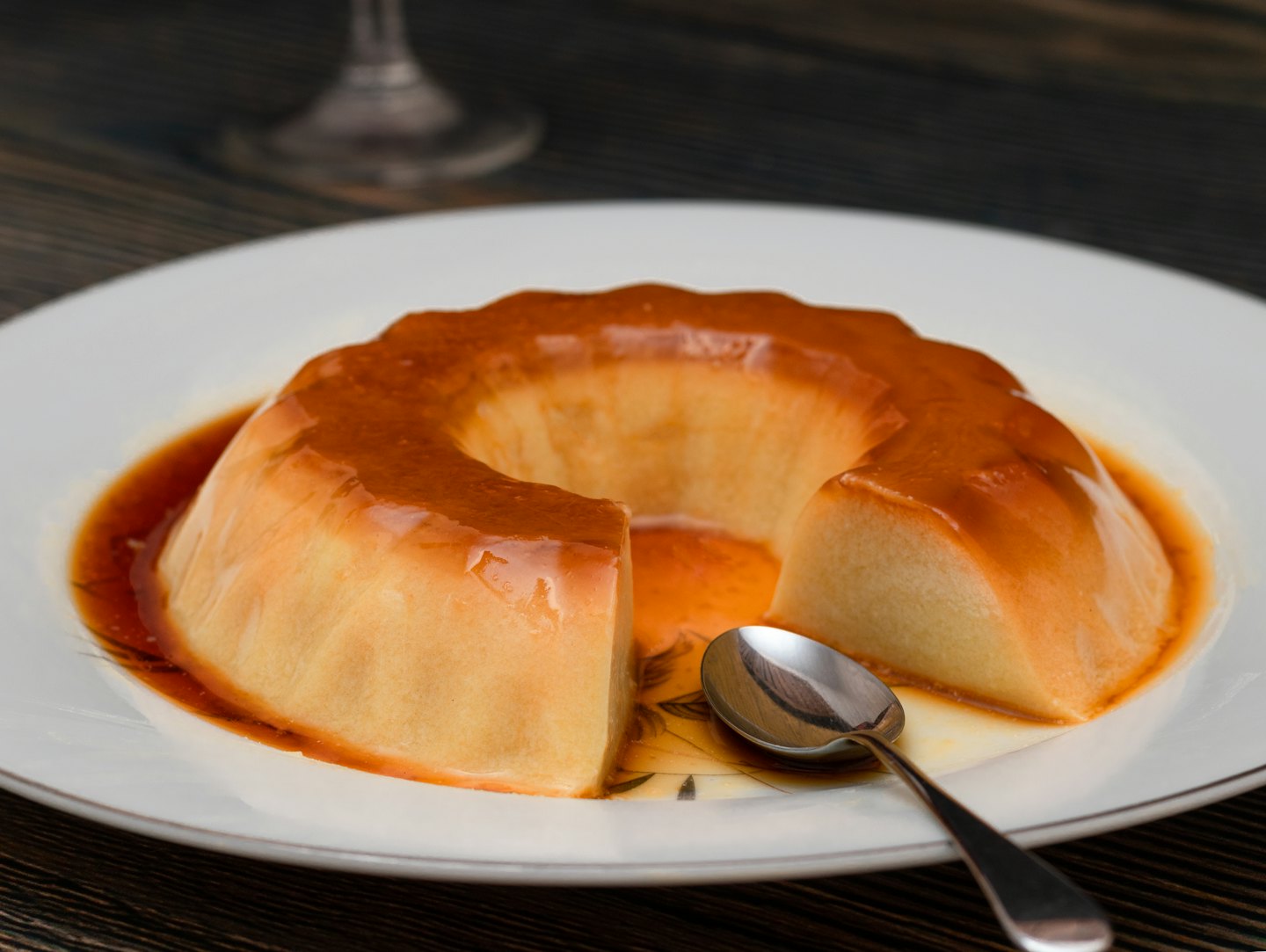 A sliced flan dessert sits on a plate with a spoon.