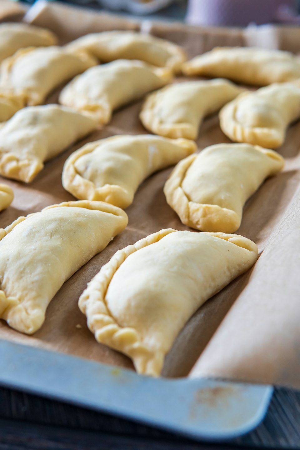 Uncooked empanadas arranged on a parchment-lined baking sheet.