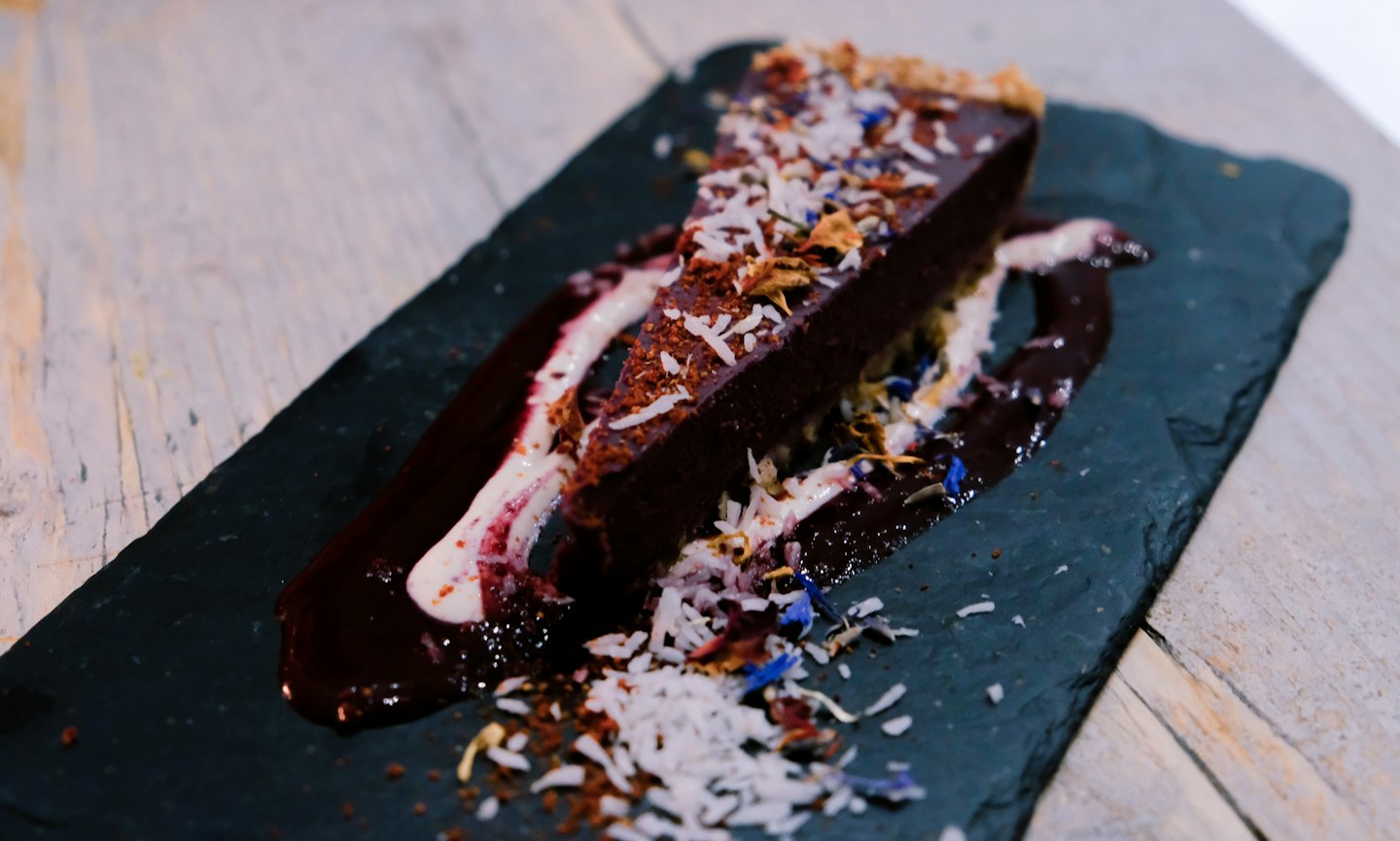 Dark chocolate tart with coconut, cornflower petals, and berry coulis.